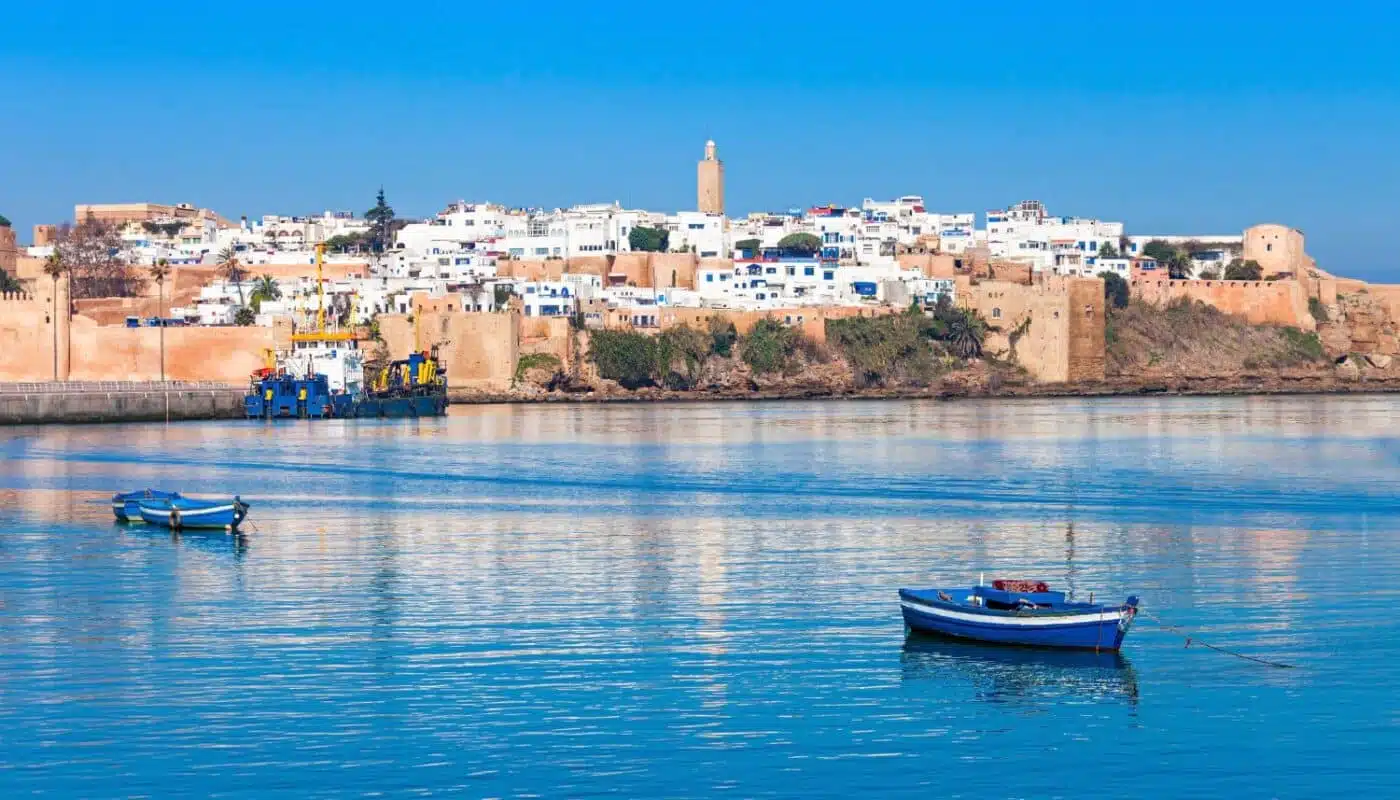 Coastal view of Rabat, Morocco, featuring the Kasbah of the Udayas and serene blue water with fishing boats in the foreground.