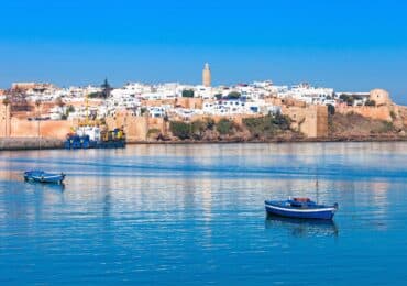 Coastal view of Rabat, Morocco, featuring the Kasbah of the Udayas and serene blue water with fishing boats in the foreground.