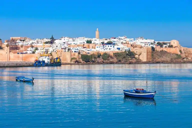 Coastal view of Rabat, Morocco, featuring the Kasbah of the Udayas and serene blue water with fishing boats in the foreground.