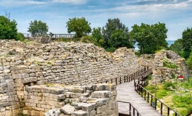 Stone seating and wooden stage of the ancient theater in the archaeological site of Troy, surrounded by trees