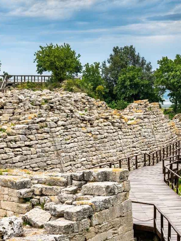 Stone seating and wooden stage of the ancient theater in the archaeological site of Troy, surrounded by trees