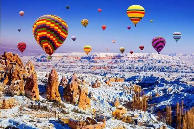 Vibrant hot air balloons soar over Cappadocia's snowy fairy chimneys and rugged landscape, creating a breathtaking winter scene.