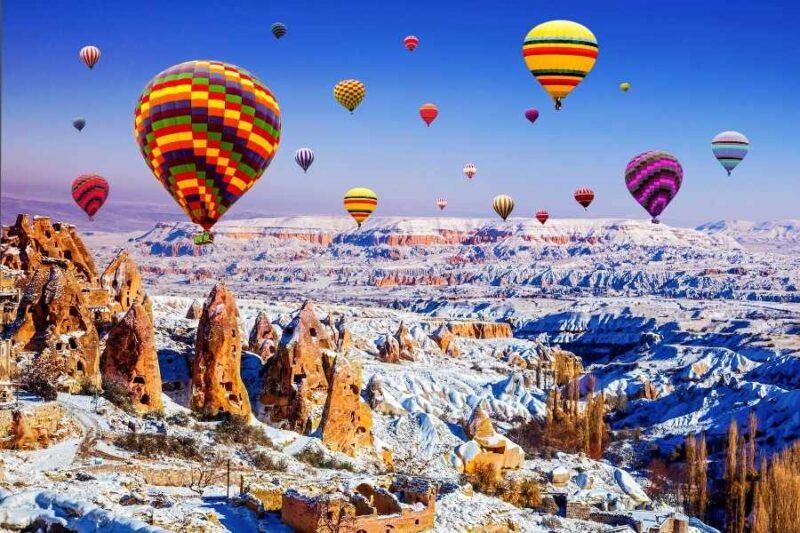 Vibrant hot air balloons soar over Cappadocia's snowy fairy chimneys and rugged landscape, creating a breathtaking winter scene.