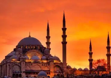 Suleymaniye Mosque in Istanbul silhouetted against a vibrant orange sunset, showcasing its grand domes and towering minarets.