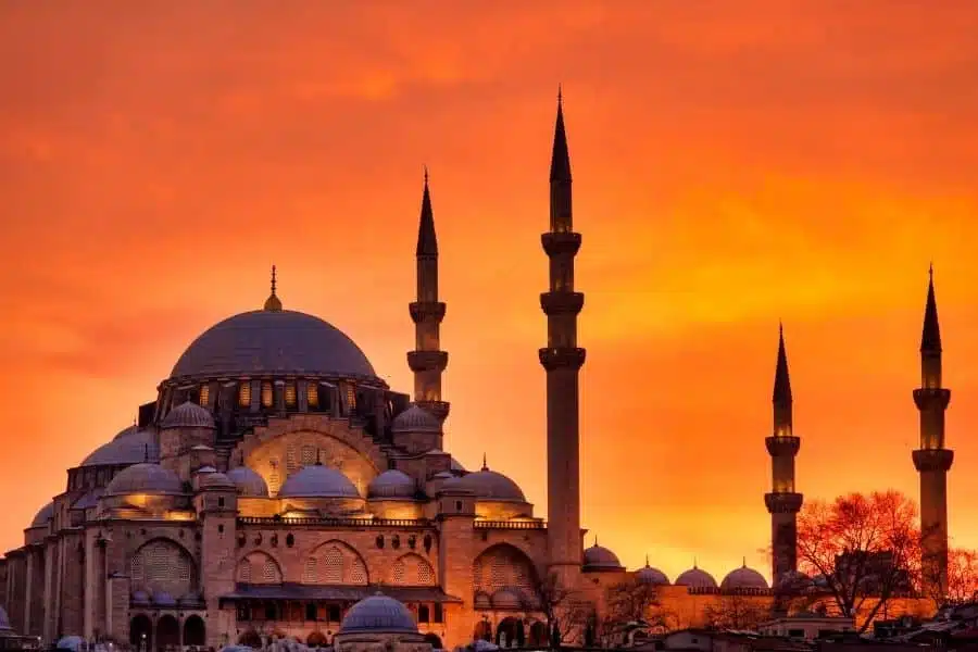 Suleymaniye Mosque in Istanbul silhouetted against a vibrant orange sunset, showcasing its grand domes and towering minarets.