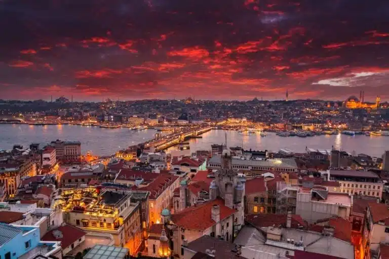 Aerial view of Istanbul with Galata Bridge and Bosphorus under a dramatic red sunset sky, lights glowing across the city.