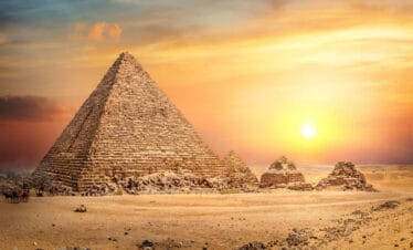 Great Pyramid of Giza in Egypt illuminated by a golden sunset, with smaller surrounding pyramids and desert landscape.