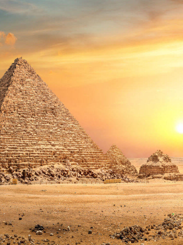 Great Pyramid of Giza in Egypt illuminated by a golden sunset, with smaller surrounding pyramids and desert landscape.