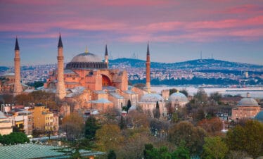 Historic Hagia Sophia mosque with domes and minarets under a pink sunset sky in Istanbul, Turkey.