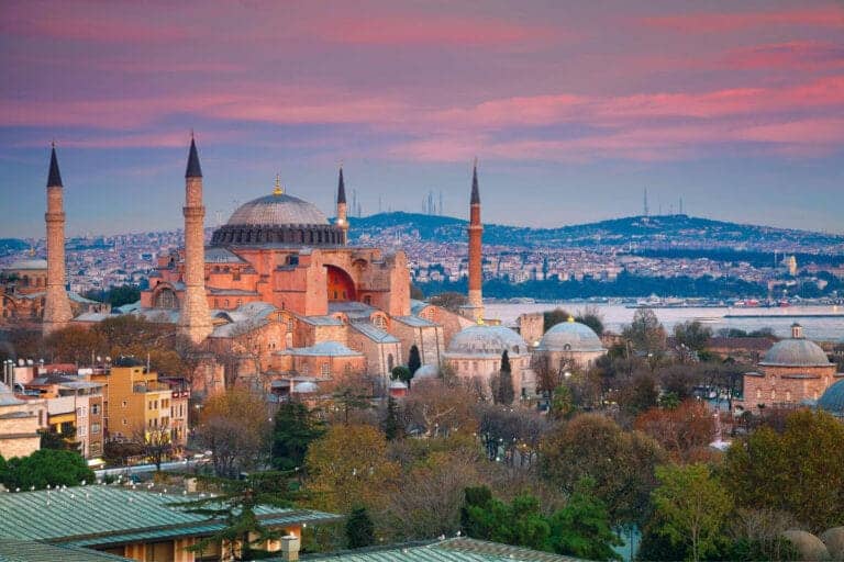 Historic Hagia Sophia mosque with domes and minarets under a pink sunset sky in Istanbul, Turkey.
