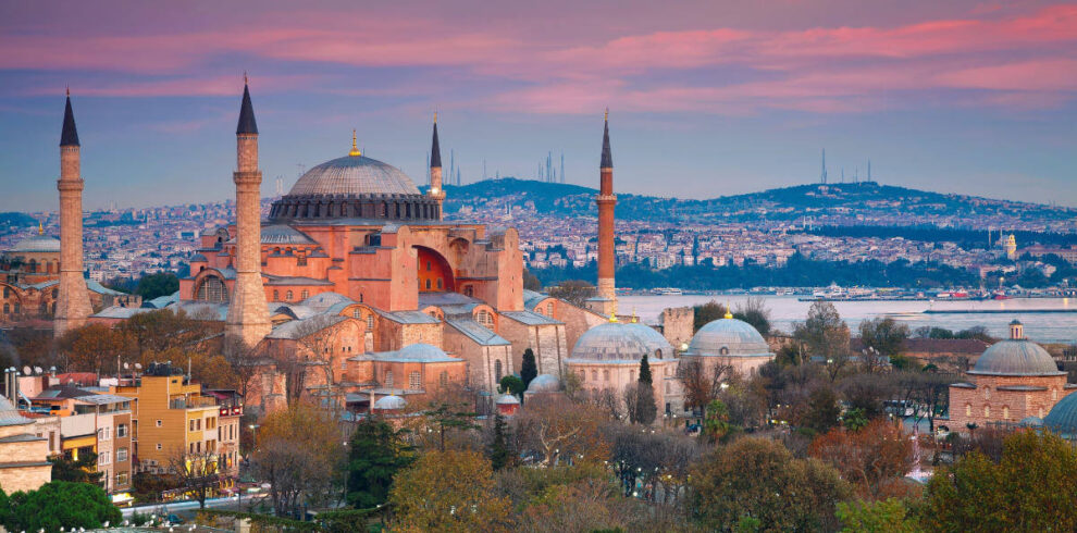 Historic Hagia Sophia mosque with domes and minarets under a pink sunset sky in Istanbul, Turkey.