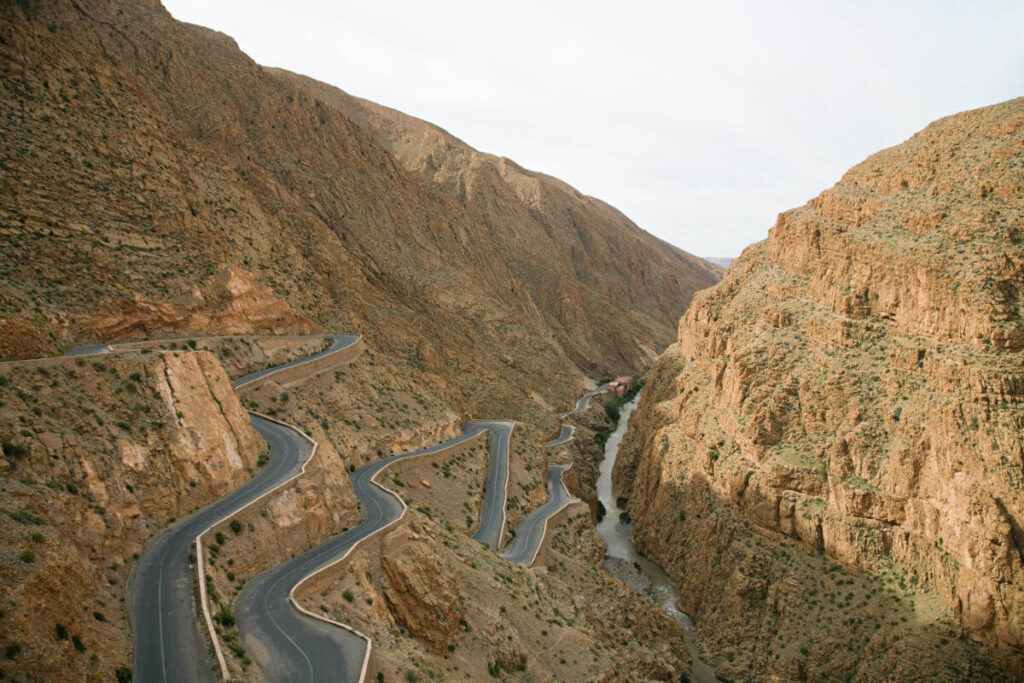 Twisting mountain road winding through steep rocky canyon with a river flowing in the valley below.