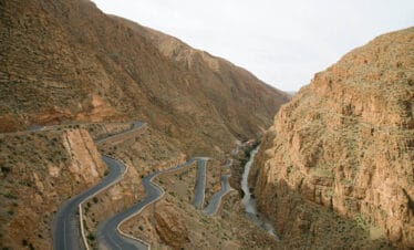 Twisting mountain road winding through steep rocky canyon with a river flowing in the valley below.