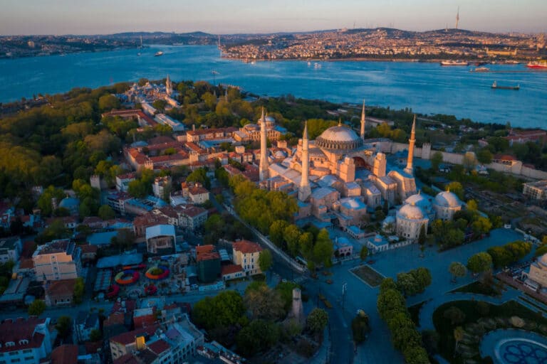 Aerial view of Hagia Sophia in Istanbul near the Bosphorus, with domes and minarets surrounded by green trees at sunset.