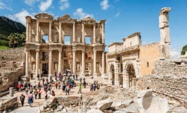 Tourists exploring the grand façade of the ancient Library of Celsus in Ephesus with clear blue skies above.
