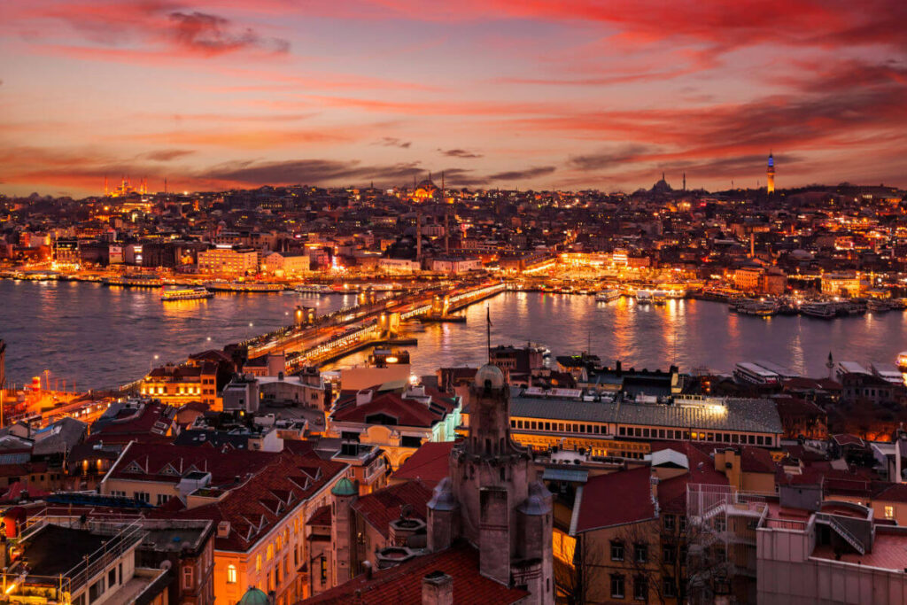 Vibrant sunset over Istanbul's Golden Horn, showcasing illuminated cityscape, Galata Bridge, and iconic mosques.