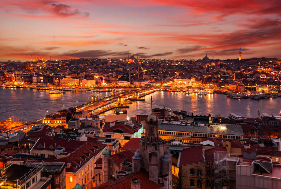 Vibrant sunset over Istanbul's Golden Horn, showcasing illuminated cityscape, Galata Bridge, and iconic mosques.