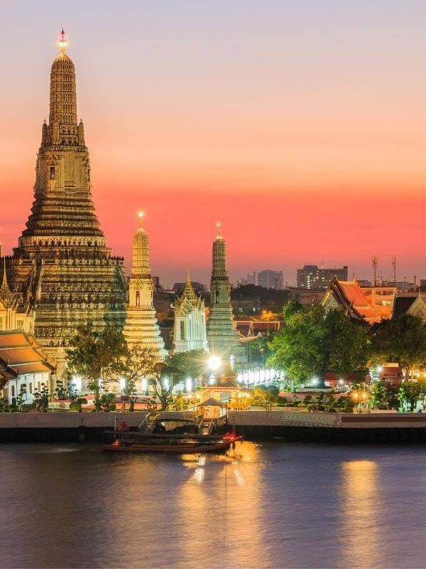 Wat Arun temple illuminated at sunset along the Chao Phraya River in Bangkok, Thailand.
