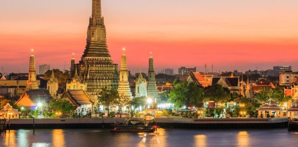 Wat Arun temple illuminated at sunset along the Chao Phraya River in Bangkok, Thailand.