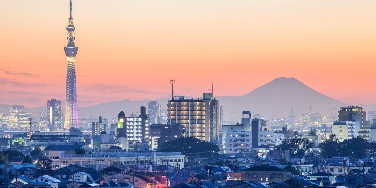 Tokyo city skyline at sunset with illuminated Tokyo Skytree and Mount Fuji in the background.