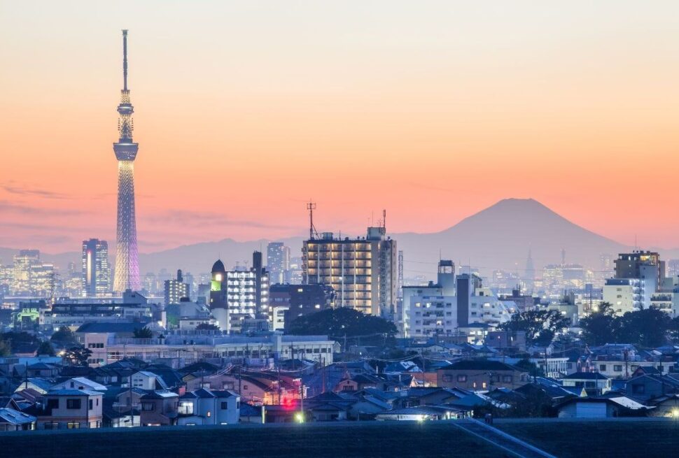 Tokyo city skyline at sunset with illuminated Tokyo Skytree and Mount Fuji in the background.