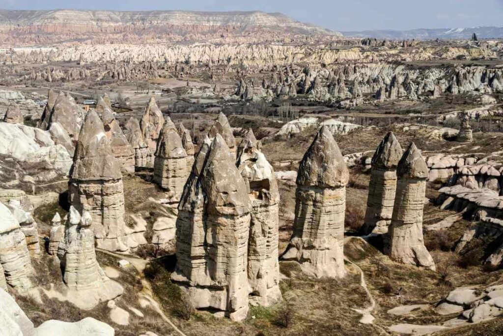 Unique cone-shaped rock formations known as fairy chimneys rise from Cappadocia’s arid valley under clear skies.