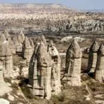 Unique cone-shaped rock formations known as fairy chimneys rise from Cappadocia’s arid valley under clear skies.