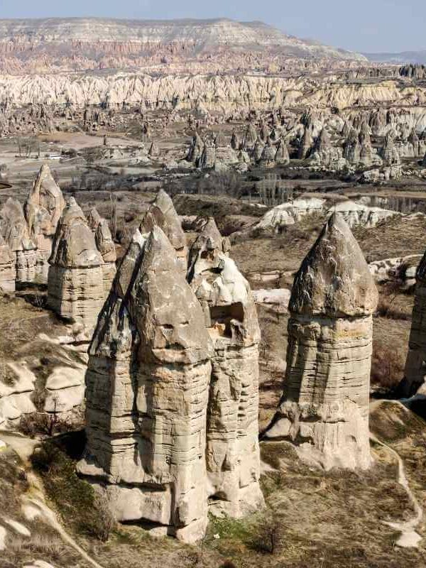 Unique cone-shaped rock formations known as fairy chimneys rise from Cappadocia’s arid valley under clear skies.