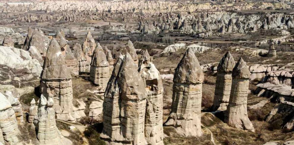 Unique cone-shaped rock formations known as fairy chimneys rise from Cappadocia’s arid valley under clear skies.