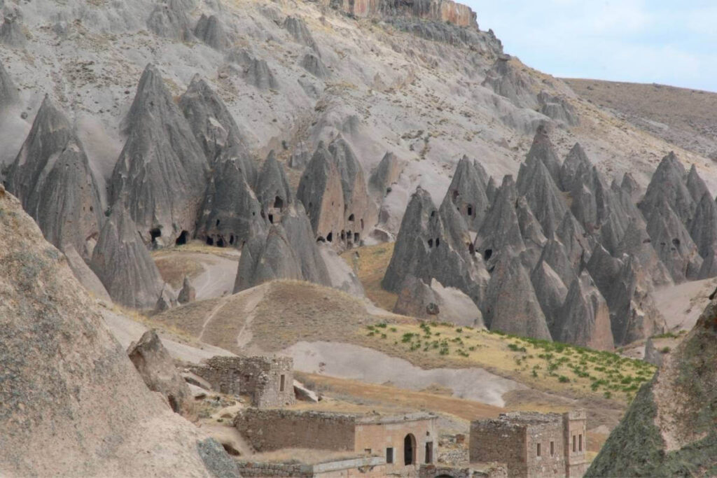 Historic cave homes carved into conical rock formations in Soğanlı Valley, Cappadocia, surrounded by arid hills.