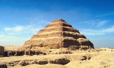 Ancient Step Pyramid of Djoser in Saqqara, Egypt, made of limestone and surrounded by desert ruins.