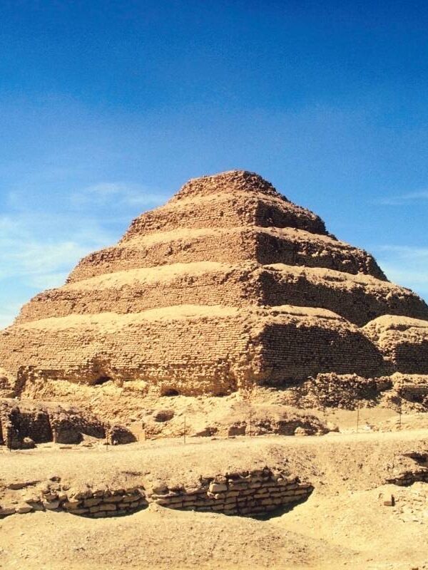 Ancient Step Pyramid of Djoser in Saqqara, Egypt, made of limestone and surrounded by desert ruins.