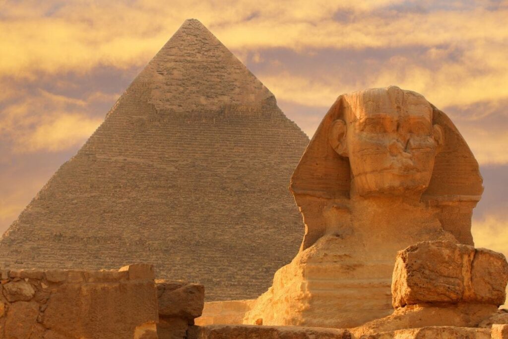 The Great Sphinx of Giza in front of the Pyramid of Khafre under a golden sunset sky in Egypt.