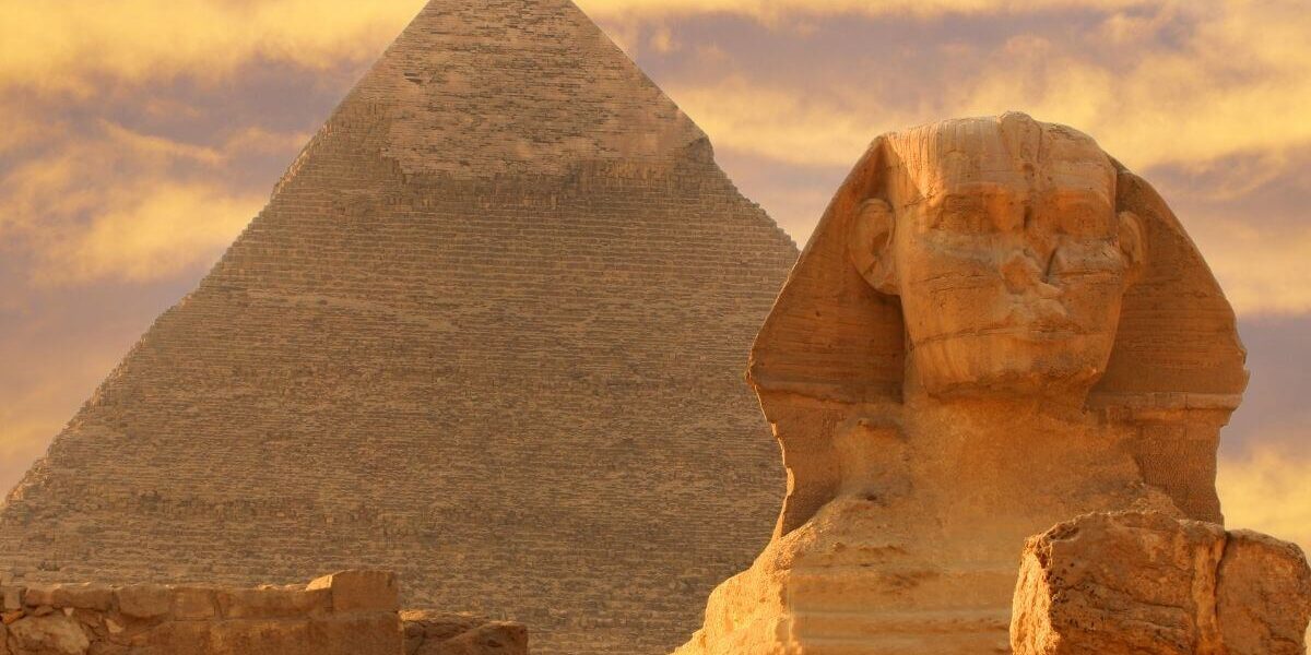The Great Sphinx of Giza in front of the Pyramid of Khafre under a golden sunset sky in Egypt.