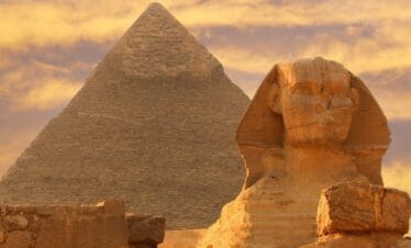 The Great Sphinx of Giza in front of the Pyramid of Khafre under a golden sunset sky in Egypt.