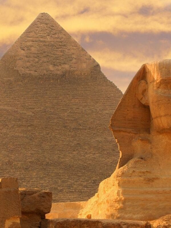 The Great Sphinx of Giza in front of the Pyramid of Khafre under a golden sunset sky in Egypt.
