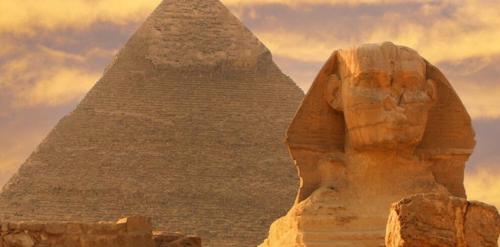 The Great Sphinx of Giza in front of the Pyramid of Khafre under a golden sunset sky in Egypt.