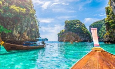 Traditional Thai longtail boats float on turquoise waters near limestone cliffs in a tropical Thailand bay.