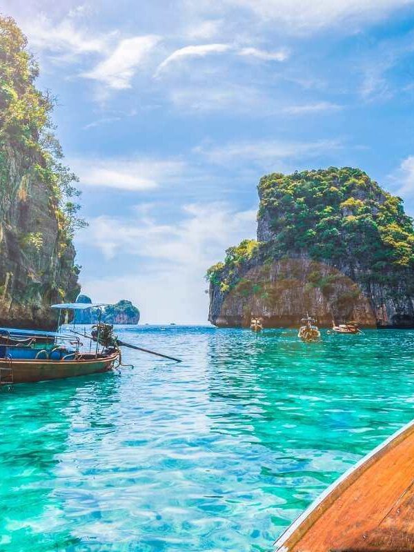 Traditional Thai longtail boats float on turquoise waters near limestone cliffs in a tropical Thailand bay.