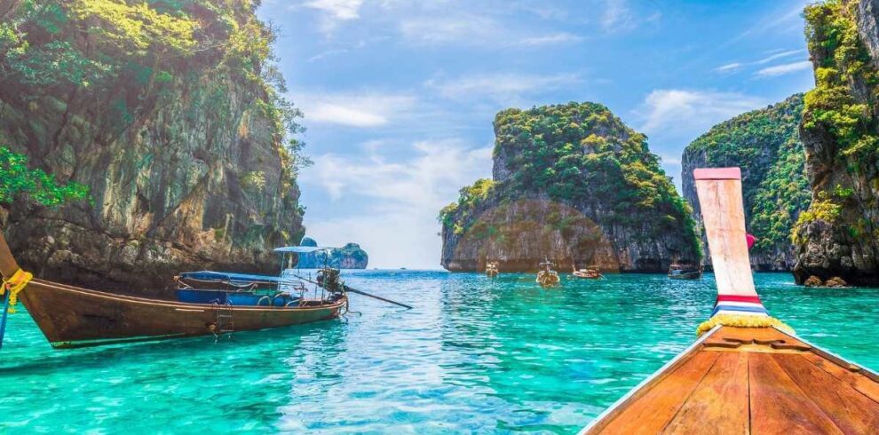 Traditional Thai longtail boats float on turquoise waters near limestone cliffs in a tropical Thailand bay.