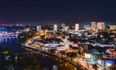 Chiang Mai cityscape illuminated at night with glowing lights, temples, and mountains in the background, Thailand.