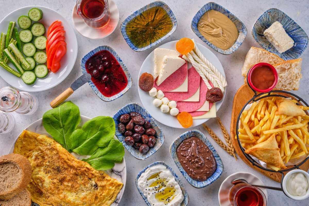 Assorted Turkish breakfast items including cheeses, olives, fries, omelet, jams, and tea arranged on a bright tabletop.