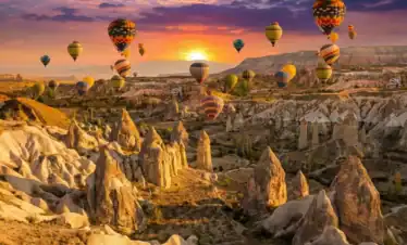 Stunning sunrise view of hot air balloons flying over fairy chimneys in Cappadocia, taken from a traditional rooftop terrace. A highlight of best Cappadocia tours.