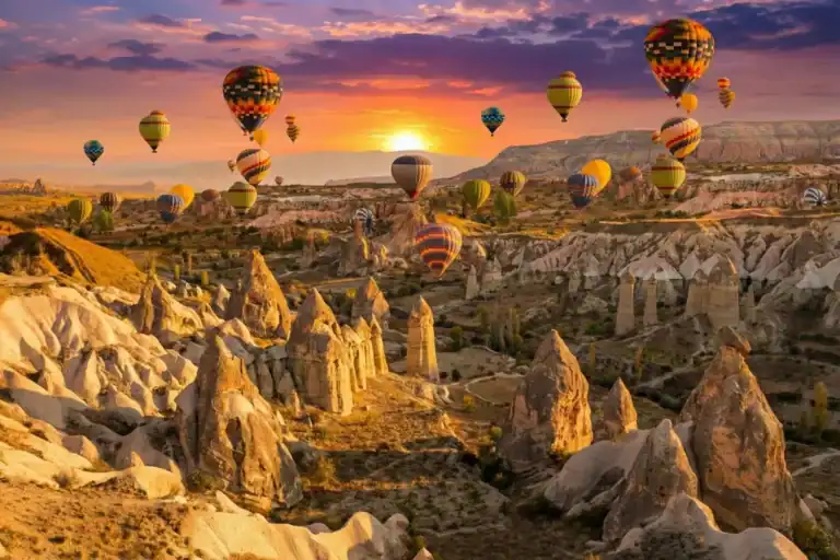 Stunning sunrise view of hot air balloons flying over fairy chimneys in Cappadocia, taken from a traditional rooftop terrace. A highlight of best Cappadocia tours.