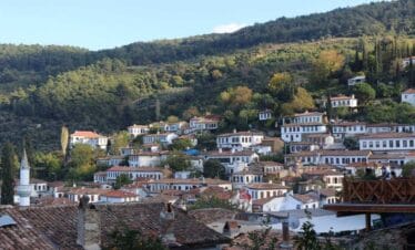 Traditional white stone houses with red-tiled roofs in Şirince Village, Turkey, surrounded by lush green hills.
