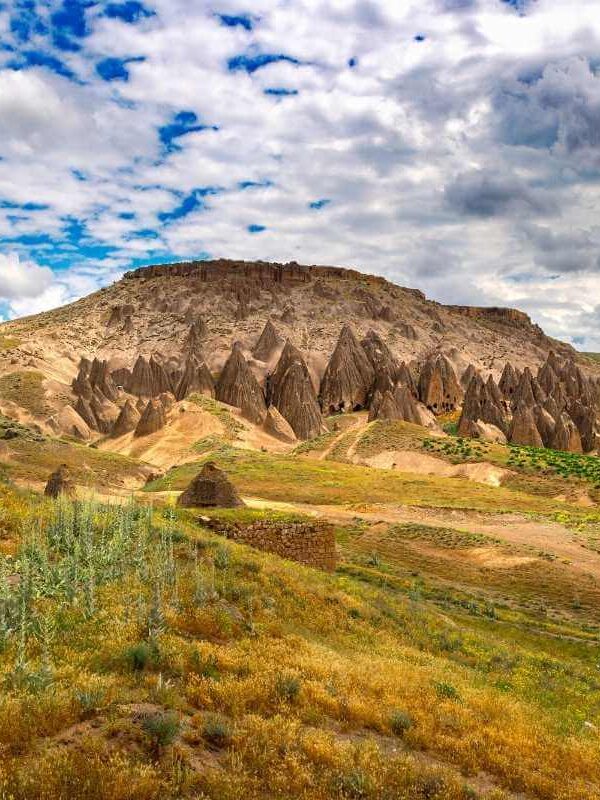Unique rock formations and cave dwellings carved into hillsides in Yaprakhisar under a partly cloudy sky.