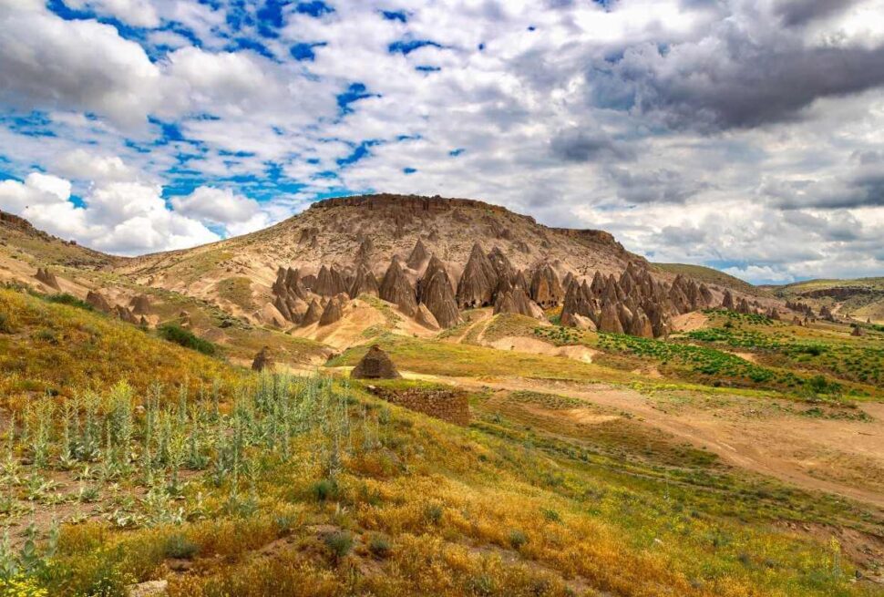 Unique rock formations and cave dwellings carved into hillsides in Yaprakhisar under a partly cloudy sky.