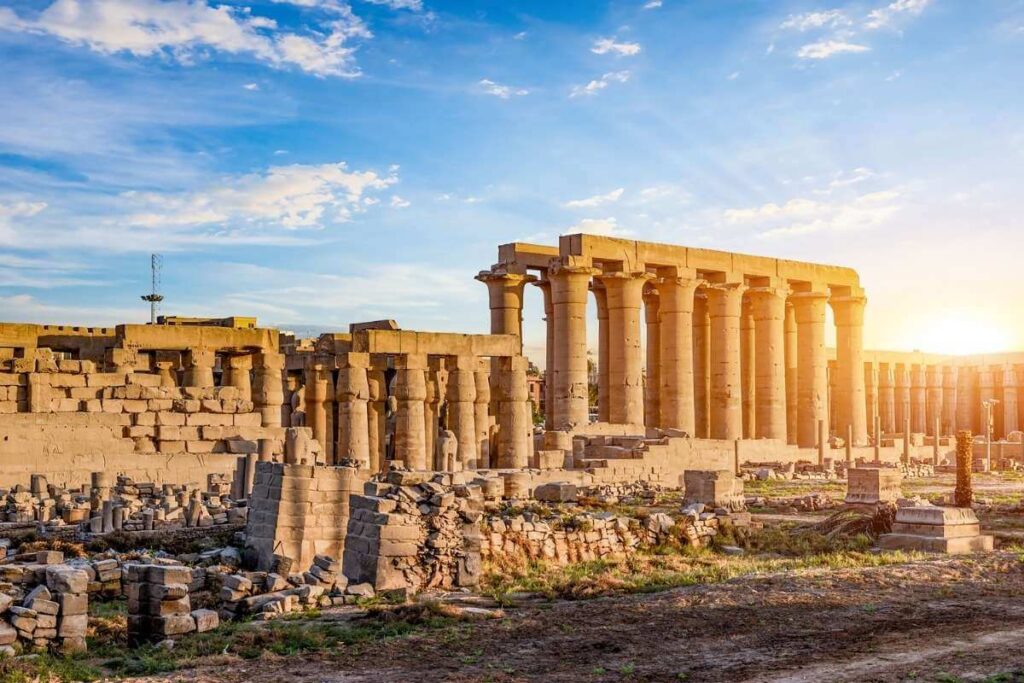Ancient Karnak Temple ruins with tall stone columns and scattered remains under a bright sunset sky in Luxor, Egypt.