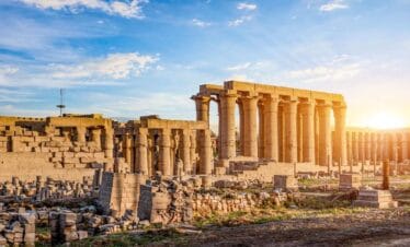 Ancient Karnak Temple ruins with tall stone columns and scattered remains under a bright sunset sky in Luxor, Egypt.