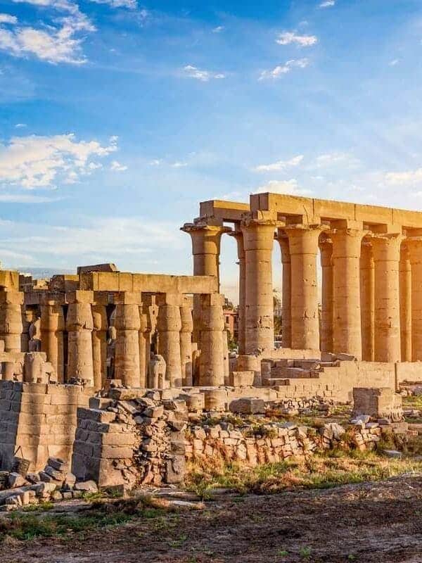 Ancient Karnak Temple ruins with tall stone columns and scattered remains under a bright sunset sky in Luxor, Egypt.